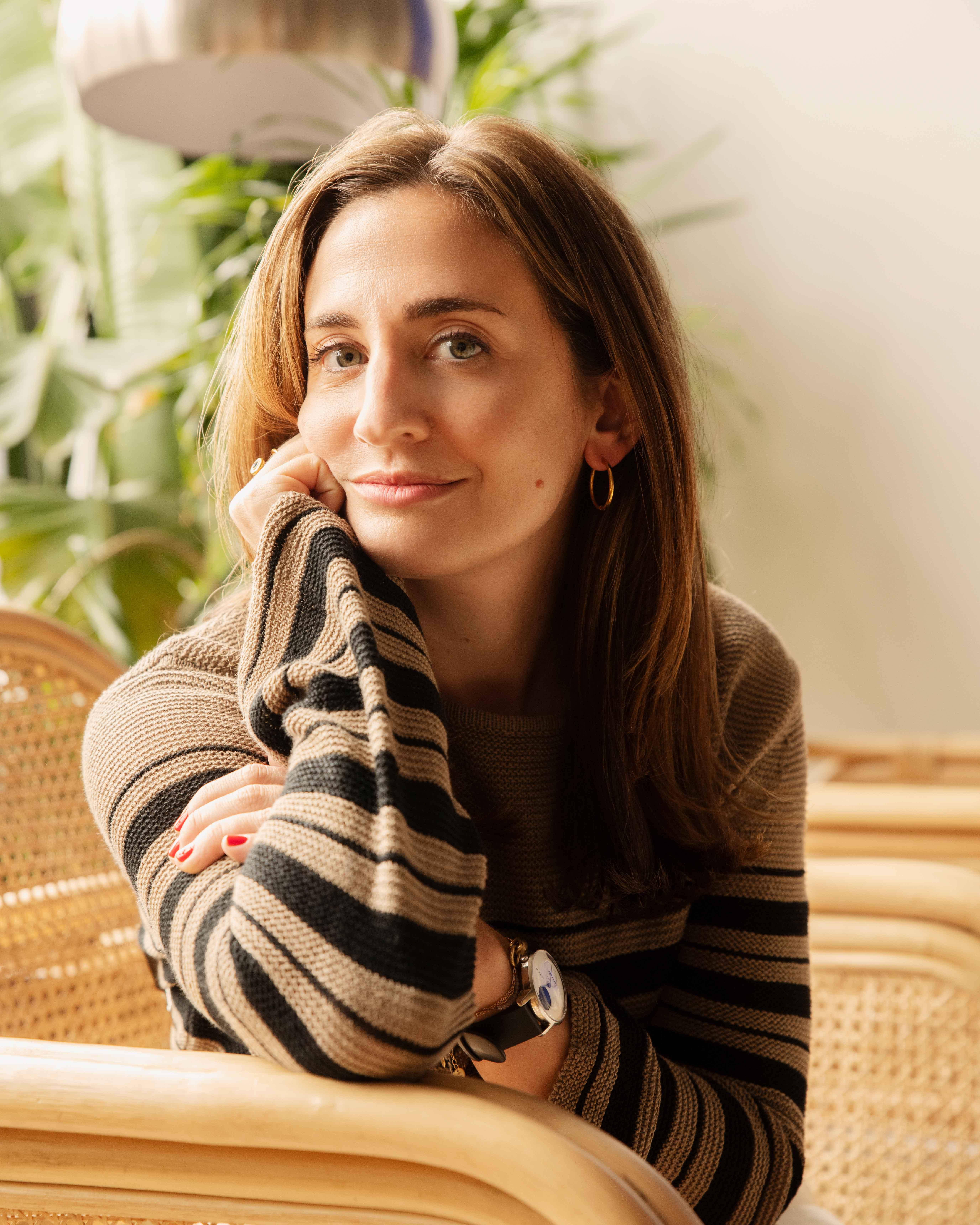 Callie Kant, Vice President of Brand and Creative at M.M.LaFleur, thoughtfully sitting in a chair with her hand on her chin, wearing a striped sweater