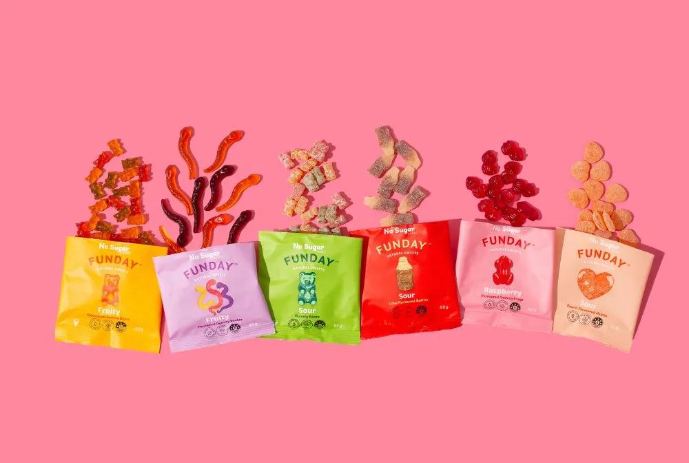 A colorful display of various bags of gummy bears arranged in a row against a vibrant pink background, representing a consumer packaged goods product in the confectionery category.