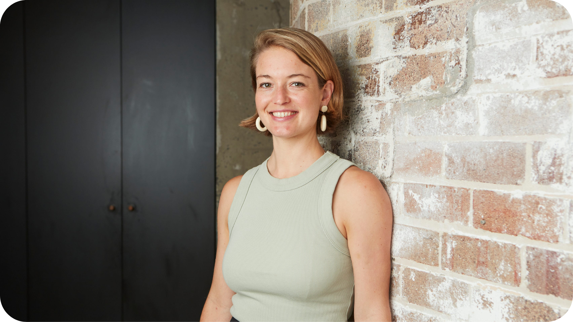 A happy woman leaning against a brick wall, symbolizing the confidence and success of a business in brand tracking and investment growth