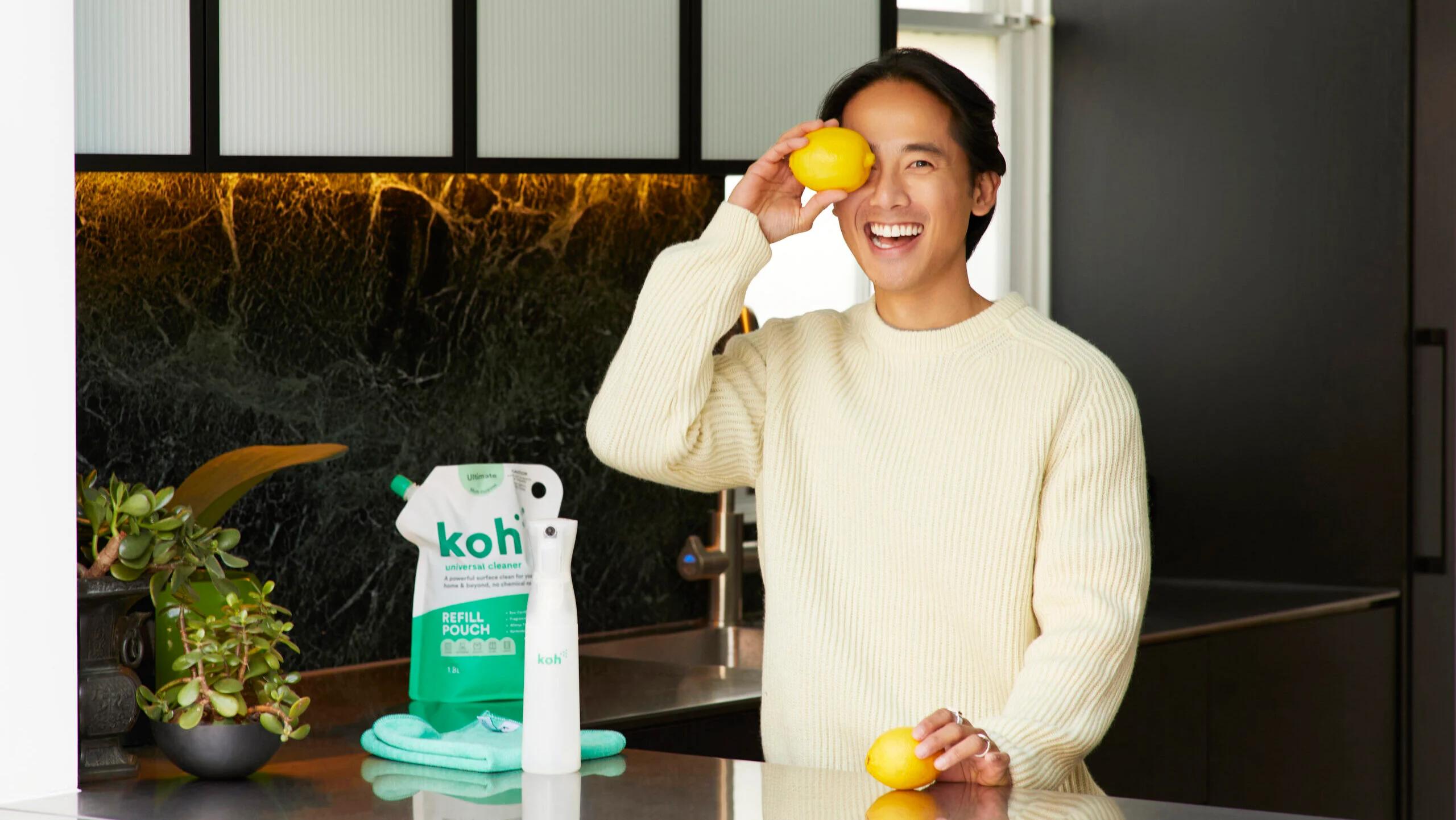 A man playfully holding a lemon in front of his eye in a kitchen, symbolizing the fun and eco-friendly approach of Koh's cleaning products