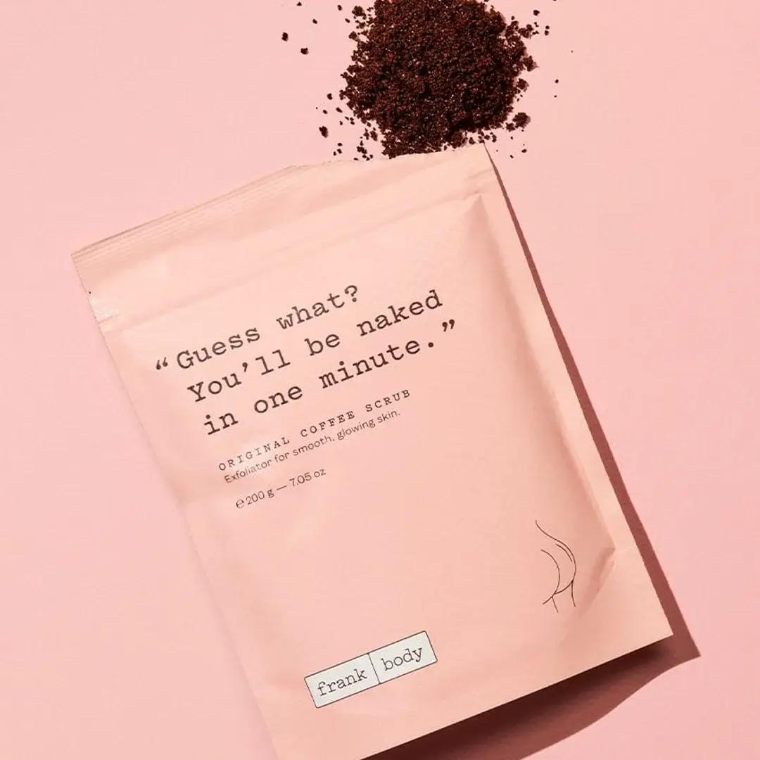 A bag of Frank Body Original Coffee Scrub placed on a pink surface, representing a consumer packaged goods product in the personal care category.