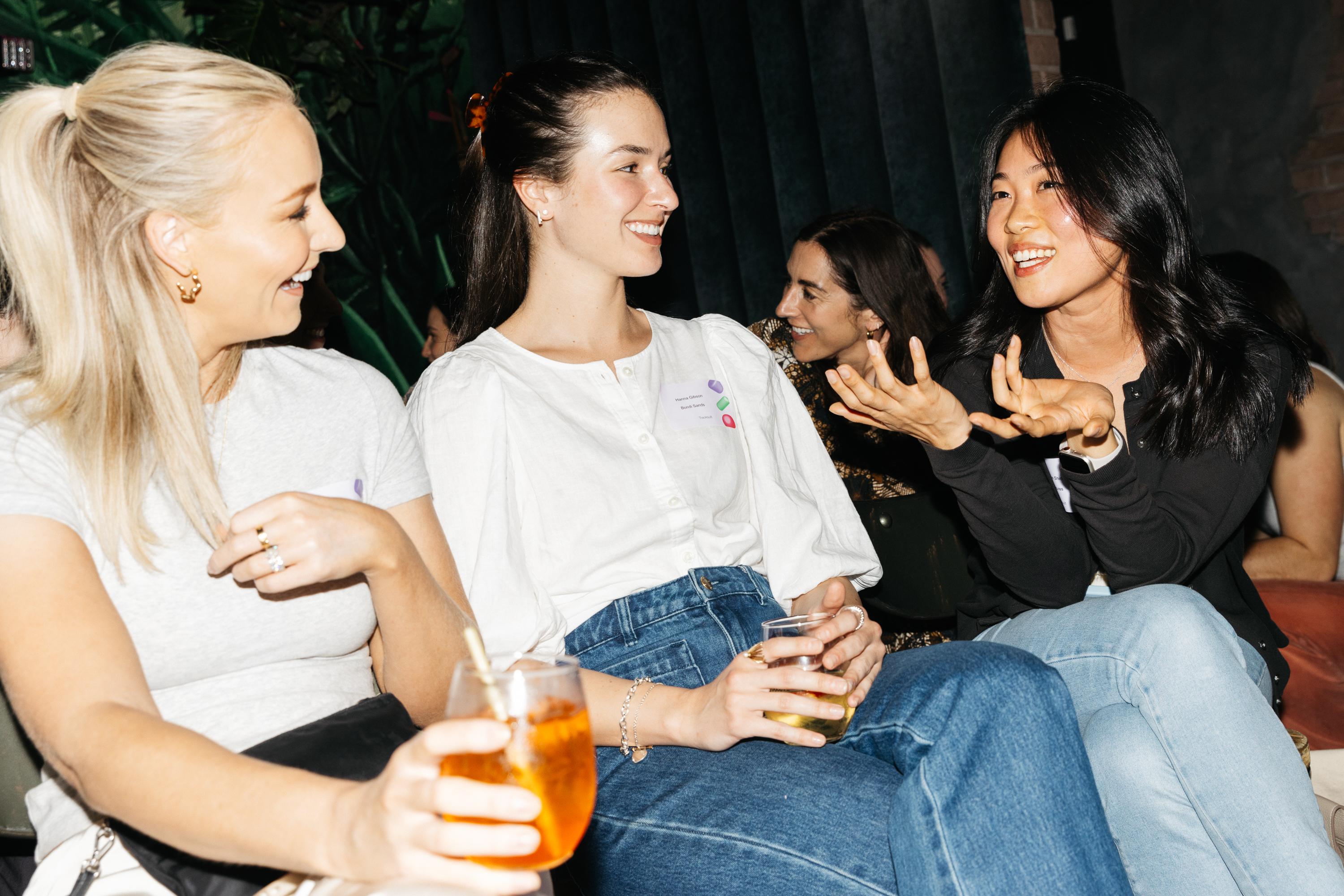 A group of women engaged in a lively discussion during the 'Building Brands of the Future' event in NYC, holding drinks and sharing insights about brand and community development strategies.
