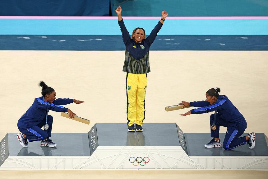 A victorious woman standing on a podium at the 2024 Olympics with her arms raised in celebration
