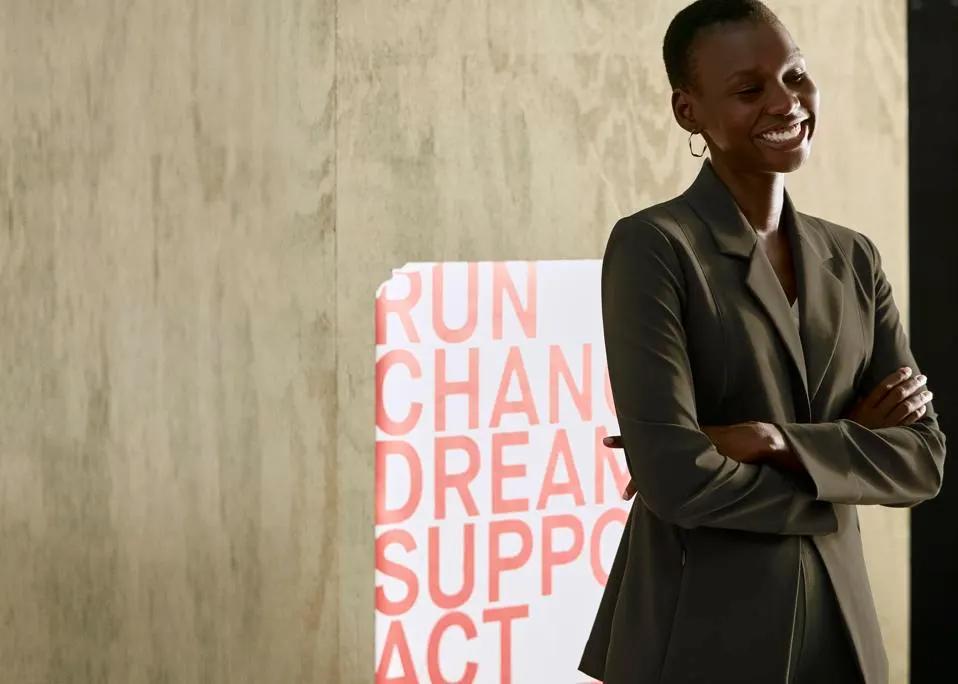 Maria Costa, Director of Brand and Integrated Marketing at M.M.LaFleur, standing confidently with crossed arms in front of a promotional poster