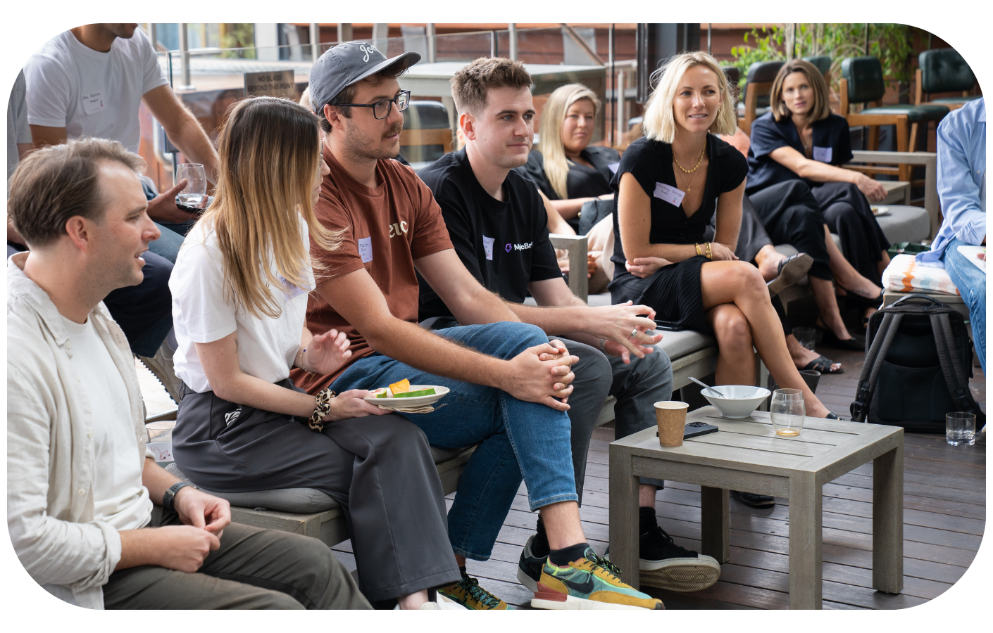 A group of professionals engaged in a discussion at a marketing event, with one man wearing a shirt with the letter 'A' on it, symbolizing the collaborative nature of brand building discussions.