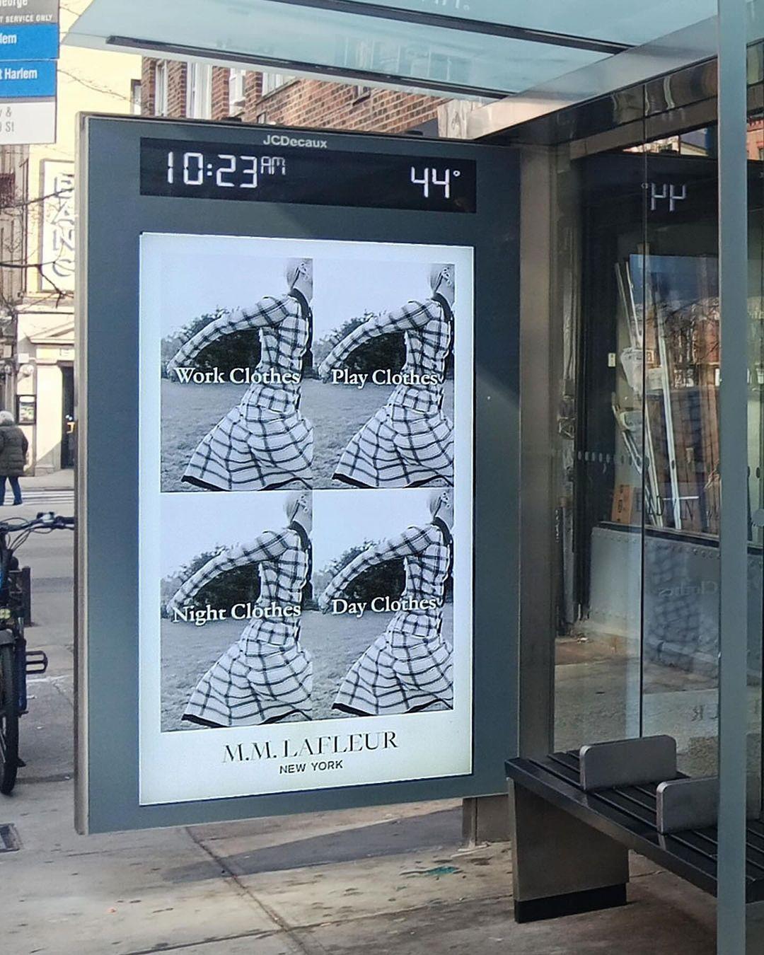 A promotional sign at a bus stop for M.M.LaFleur, advertising their range of work clothes, play clothes, and night clothes, reflecting the brand's expansion beyond professional workwear.