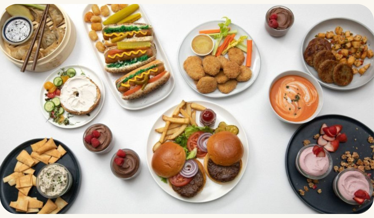 A table filled with a variety of food items including hot dogs and hamburgers, showcasing the versatility of Nature's Fynd meat and dairy alternatives made from nutritious fungi protein.